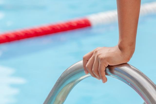 Kinderhand auf einer Einstiegsleiter in ein Freibad